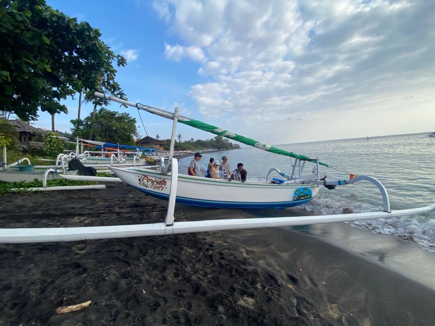 Guests boarding a jukung at eye level, outriggers crossing the frame